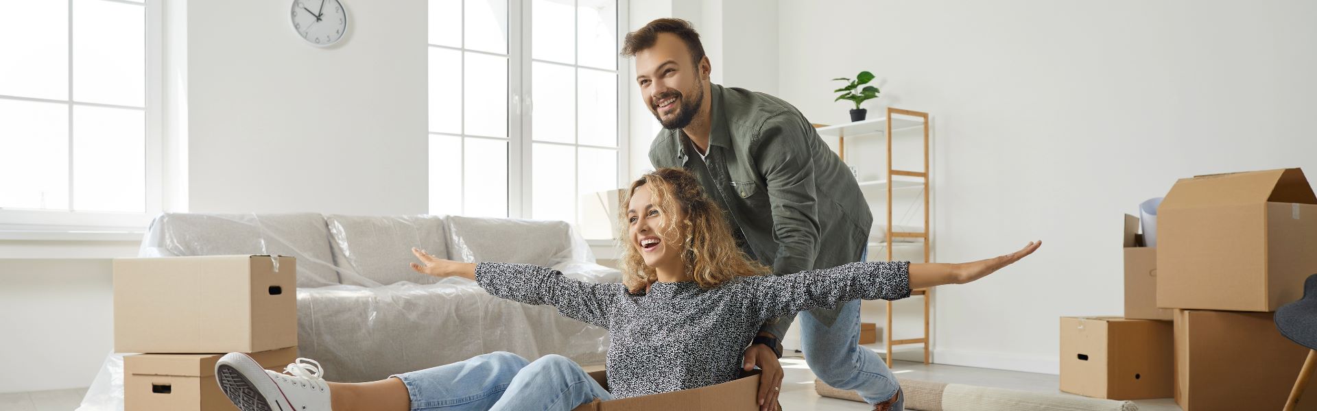Un homme poussant joyeusement sa femme assise dans une boîte en carton pendant leur déménagement après avoir vendu leur bien immobilier à Anglet.