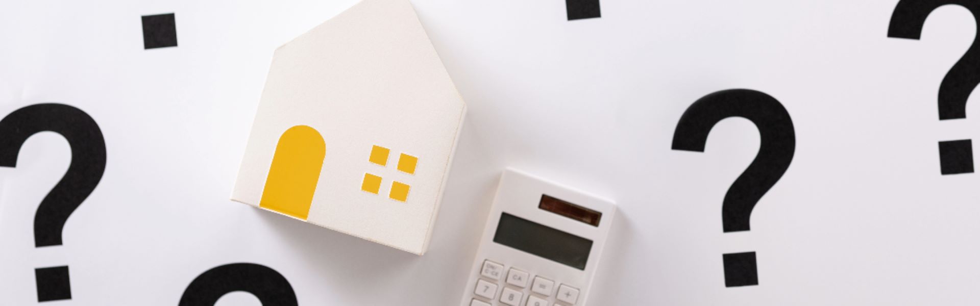 Une maison en bois et une calculatrice entourés de points d'interrogation pour illustrer quels sont les frais à prévoir lors d'un achat immobilier