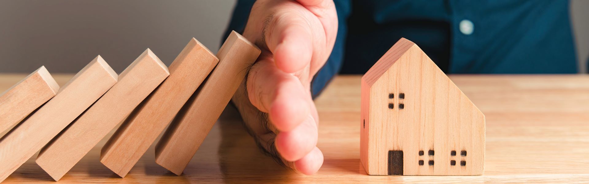 Main protégeant une maison en retenant des blocs qui s'effondrent comme des dominos, symbole de garantie et de protection pour un prêt immobilier.